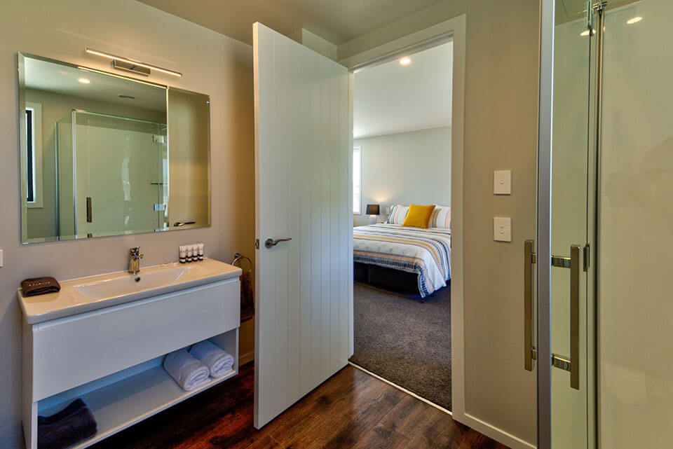 Perspective from the bathroom with white vanity unit shown and looking back through the door to the bedroom of motel unit.