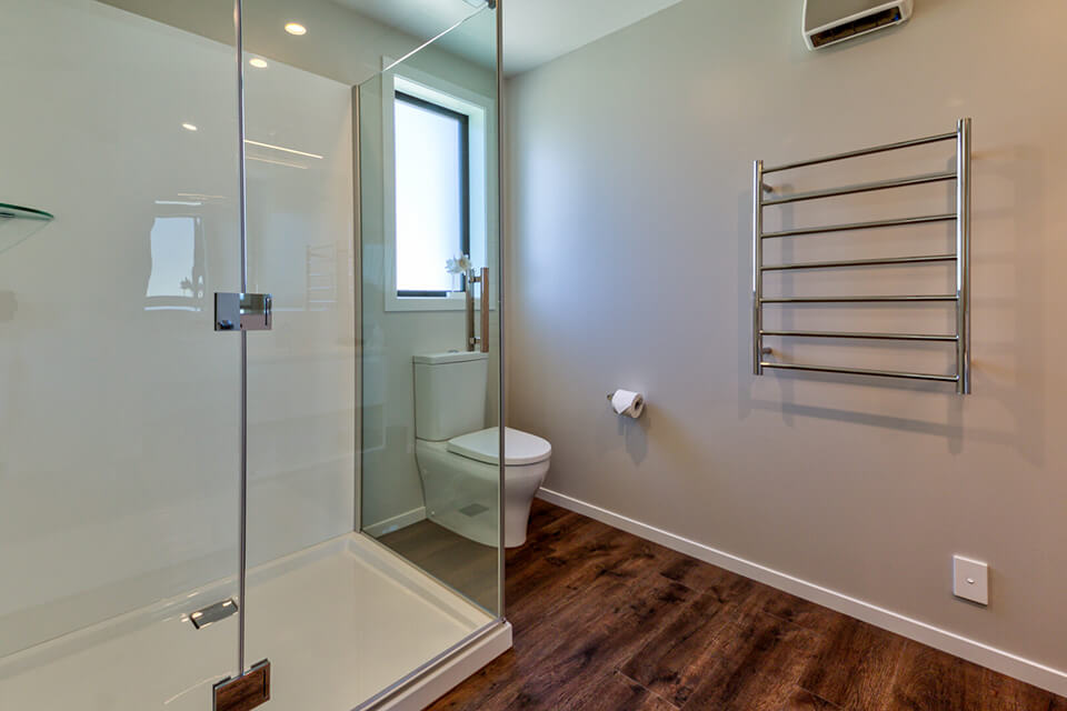 Bathroom setting with a glass-doored shower, toilet and heated towel rail.
